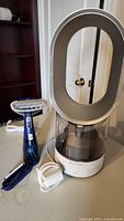 Dyson humidifier with loop amplifier and clear water tank alongside Conair handheld steamer and power cords