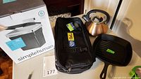 Photo showing Simplehuman 10L trash can box, black chef cutter kit carrier bag, copper-colored whistling kettle, and Lodge cast iron grill pan.
