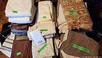 Photo showing multiple folded bed linens including cream, brown, and multicolored paisley duvet covers with labeled tags.