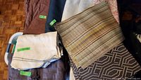 Assortment of folded tablecloths and placemats in earthy and neutral tones with green size labels visible