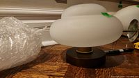 Side view of one light fixture with frosted glass globe and brass-tone metal base, next to bubble wrap.
