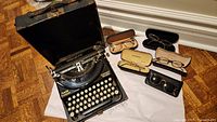 1930s Smith Premier Compact Portable typewriter next to four pairs of glasses and sunglasses, all in cases