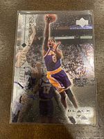 Front of 1998-99 Upper Deck Black Diamond Kobe Bryant basketball card showing Kobe Bryant in purple/yellow LA Lakers uniform mid-air with crowd background.