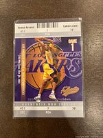 Front of the 2003-04 Fleer Authentix Kobe Bryant basketball card showing player in action with Lakers logo and game info.