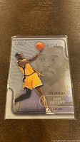 Photo of the front side of the 2003-04 Fleer Flair Kobe Bryant basketball card #4, showing Kobe in mid-air against a silver background and a large faded portrait of him.