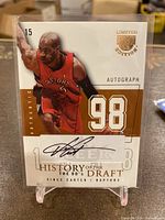 Front of card in plastic sleeve on clear stand showing full-color image, autograph and limited edition foil accents