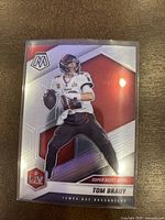 Front image of glossy 2021 Panini Mosaic football trading card showing Tom Brady in a Tampa Bay Buccaneers uniform prepping to throw a football. Features holographic silver and red design with Super Bowl LV logo and MVPs text.