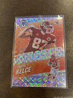 Front view of one 2021 Panini Mosaic Travis Kelce Got Game Mosaic PRIZM Insert football card with shiny orange holographic mosaic pattern.