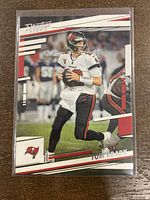 Front of 2022 Panini Prestige Tom Brady football card showing Brady in mid-play in Tampa Bay Buccaneers uniform with design elements and card branding.
