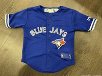 Front view of the blue Blue Jays kids jersey with button closure, Blue Jays logo, and 'BLUE JAYS' text. Shows patch wear.