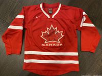 Red Nike Team Canada hockey jersey for kids size 6 laid flat showing front with maple leaf Team Canada crest and white stripe details