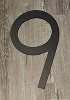 Matte black metal house number 9 hanging on wooden floor