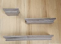 Top view of three grey wood-grain composite shelves arranged on wooden floor showing size differences.
