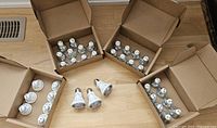 Cardboard boxes open showing multiple halogen light bulbs, and a few LED bulbs arranged on the floor.