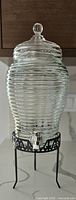 Front view of beehive shaped glass beverage dispenser on black metal stand with silver spigot and clear lid knob.