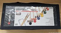 Black rectangular fabric carry bag with a clear plastic window showcasing the croquet mallets and balls inside. The bag label shows brand Gamecraft and croquet set information.