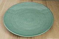 Top view of large round decorative turquoise plate on wooden floor.