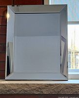 Mirror shown in vertical orientation on rustic stone shelf in front of brick wall, illuminated by natural light from window.