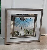 Front view of the medium sized print with blue flower and green butterfly, showing the mirrored matting and heavy metallic frame with a slight offset and slanted appearance.