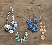 Lot overview showing all four necklaces laid flat on wood surface with various floral styles and colors.