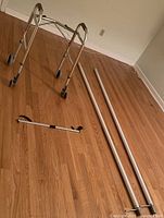 Sunrise Medical folding walker, two long sections of floor to ceiling grab pole, and reacher tool laid on wooden floor, front view.
