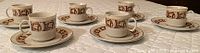 Six espresso or tea cups with matching saucers arranged on a white quilted surface.