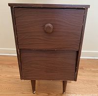 Front view of the nightstand showing drawer fronts, single round knob on top drawer, and painted wooden legs with chip wear.