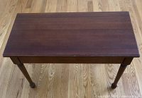 Front view showing four legs of the wooden piano bench on wooden floor.