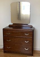 Front view of the wooden dresser with attached mirror showing drawer handles and upper surface.