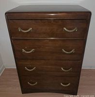 Front view of the vintage dresser showing all four drawers with curved brass handles and general wood finish.