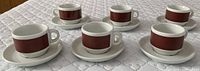 Set of six demi-tasse espresso cups with matching saucers arranged on a white surface, showing the full set with consistent design.
