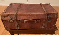 Exterior of a brown pigskin leather suitcase with leather straps and metal clasps