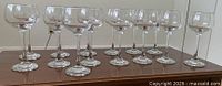 Fourteen clear glass wine glasses shown in a group on a wooden surface.