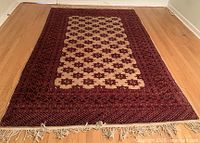 Top-down view of wool rug laid on hardwood floor showing Bukhara pattern, border and fringe