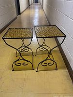 Two midcentury modern vintage nesting side tables shown side by side on floor, black wrought iron bases with detailed curves and amber textured glass tops.