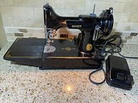 Left-front view of sewing machine on countertop showing base, extension table, needle area and connected foot pedal.