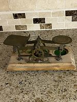 Front left angle view of the antique brass and wood postal scale showing the balance beam and wooden base with felt insets.