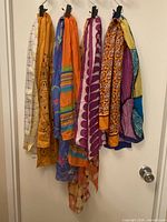 Full view of seven vintage neck scarves hanging, displaying various colors and patterns including white, orange, blue, purple, and multicolored.