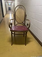 Front view of a mid-century modern bentwood armchair with oval cane backrest and burgundy reupholstered seat. Shows sculptural curved armrests and four legs.