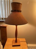 Full view of the MCM wooden table lamp with burlap shade placed on a wooden surface against a lit background.
