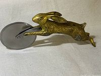 Photo showing side profile of the vintage brass bunny pizza cutter with visible detailed brass rabbit handle and stainless steel cutting wheel.