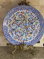 Front of the enamel decorative plate showing detailed colorful embossed style painted design with birds and floral motifs on a stand.