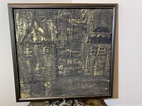 Vintage mixed media artwork in black frame showing medieval style buildings with textured surfaces and gold accents.