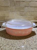 Side view of vintage Pyrex Pink Daisy oval casserole dish with glass lid on countertop.
