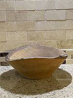 Side view of handmade maple wood bowl with bark edge rim showing natural wood grain and bowl shape on a kitchen counter.