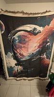 The photo shows a large rectangular wall hanging carpet with fringe edges, depicting a detailed astronaut helmet with a nebula and outer space scene inside the visor.