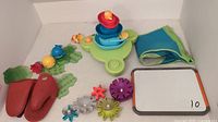 Photo of assorted bath toys including sea creatures, fountain island with stacking cups, corner suction cup bag, lobster claw oven mitts, and a small whiteboard.