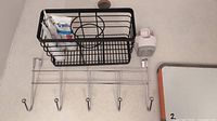 Back-of-door metal hanger with six hooks, with black metal caddy holding 3 tubes of Tom's toothpaste and white wall-mounted toothpaste dispenser on countertop.