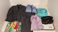 Top-down photo showing a dark gray boys suit jacket and matching pants, three dress shirts (striped blue, lavender, turquoise golf shirt), a colorful handmade Christmas vest, and a pair of black dress shoes size 10