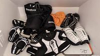 Overhead photo showing all youth hockey gear items including gloves, pants, shin guards, elbow pads, and protective gear in black, white, and orange colors arranged on the floor.